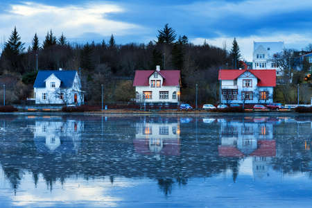 Beautiful houses reflected in lake Tjornin in Reykjavik Iceland, during the blue hour in winterの写真素材
