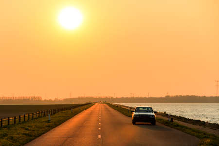 Mysterious car on the levee at sunset in the Netherlandsの写真素材