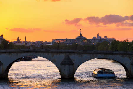 Beautiful vibrant sunset over the river Seine in Paris, France, with a tourist canalboat under an arched bridge and the Grand Palais in the backgroundの写真素材