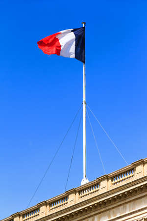 Red, white and blue french flag waving on top of a building in Parisの写真素材