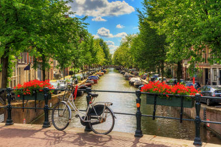Beautiful vibrant summer flowers and a bicycle on a bridge on the famous world heritage canals of Amsterdam, The Netherlandsの写真素材
