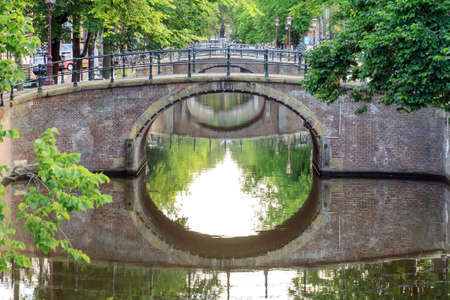 Beautiful summer morning view of the bridges over the famous Reguliersgracht canal in Amsterdam, The Netherlands, with a mirror reflectionの写真素材