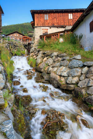 Beautiful small creek running past the ancient sawmill with water wheel in the picturesque village of Grimentz, Switzerland, in summerの写真素材