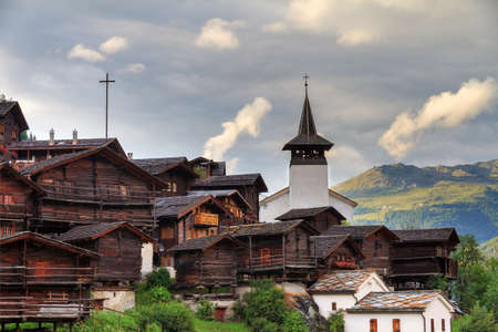 Beautiful cityscape of the alpine village Grimentz, Switzerland, with traditional wooden houses and church tower in summerの写真素材