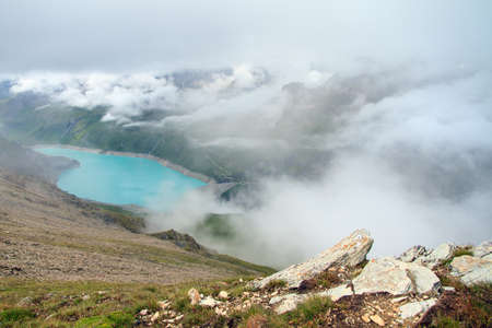 Beautiful view from above of the vibrant turquoise reservoir lake Lac de Moiry in the alps near Grimentz, Switzerland, on a cloudy summer day in the mountainsの写真素材