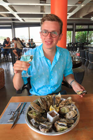 Young man with eyeglasses enjoying the taste of fresh raw oysters with white wine at the french coast of Brittany (Bretagne) in Lorient, France, on July 30, 2014のeditorial素材