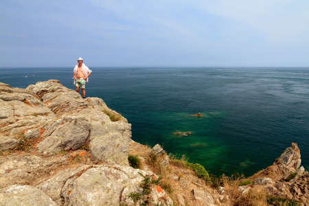 Beautiful view of a colorful young tourist on the rocks at Pointe du Grouin near Cancale in Brittany, France,  in summerの写真素材