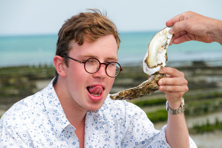 Young man enjoys the taste of a rare big oyster called a pied de cheval (horse's hoof) at the french coast of Brittany (Bretagne) in Cancale, France on a summer dayの写真素材