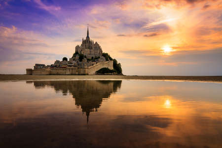 Beautiful view of historic landmark Le Mont Saint-Michel in Normandy, France, a famous UNESCO world heritage site and tourist attraction, at sunset with reflectionの写真素材