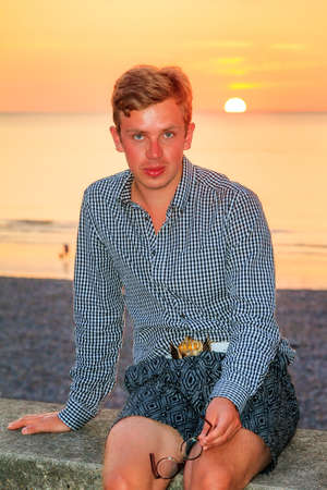 Beautiful portrait of a young caucasian man at sunset at the beach looking at the cameraの写真素材