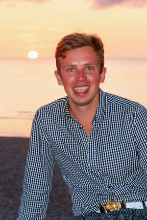 Beautiful portrait of a young caucasian man at sunset at the beach looking at the cameraの写真素材