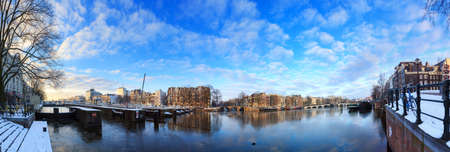 Beautiful 180 degree cityscape panorama of the river Amstel in Amsterdam, the Netherlands, in winter with ice and snow with the famous skinny bridgeの写真素材