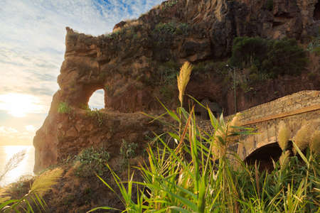 Beautiful backlit landscape view of the coastline cliffs at Tuneis antigos near Ponta do Sol on the east coast of Madeira island, at sunset with the atlantic ocean in summerの写真素材