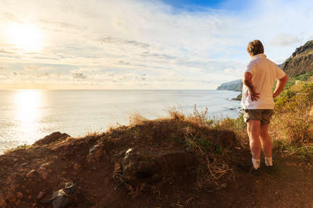 Senior tourist hiking at Tuneis antigos near Ponta do Sol on the east coast of Madeira island, at sunset with the atlantic ocean in summerの写真素材