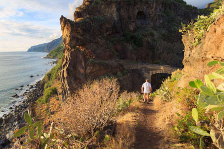 Senior tourist hiking at Tuneis antigos near Ponta do Sol on the east coast of Madeira island, at sunset with the atlantic ocean in summerの写真素材
