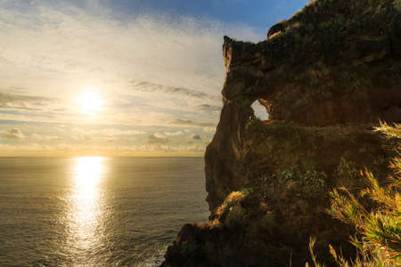 Beautiful backlit landscape view of the coastline cliffs at Tuneis antigos near Ponta do Sol on the east coast of Madeira island, at sunset with the atlantic ocean in summerの写真素材