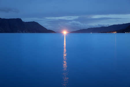 Beautiful view of the tropical tourist destination Lake Toba, Sumatra, Indonesia, in the blue hour at night, with a bright light shining on the shoreの写真素材