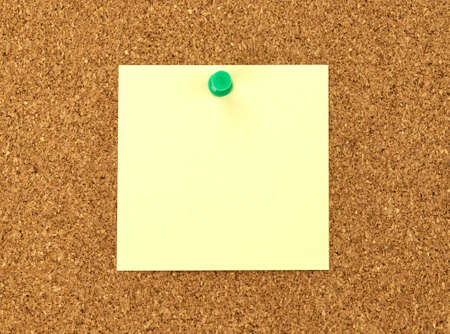 Blank yellow sticky note posted to a cork notice board.の写真素材