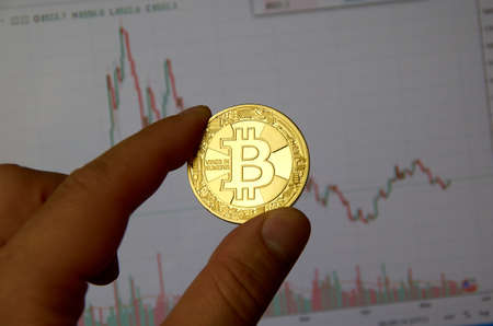 MONTREAL, CANADA - SEPTEMBER 8, 2018: A hand holding Bitcoin gold crypto currency coin in a hand over a bitcoin chart on a desktop screen.のeditorial素材