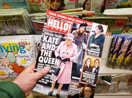 MONTREAL, CANADA - MARCH 28, 2019: Hello magazine in a hand with Queen Elizabeth on front cover over stand of different magazines in a store. Hello is a weekly magazine specializing in celebrity newsのeditorial素材