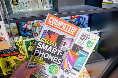 AMSTERDAM, NETHERLANDS - OCTOBER 08, 2018: Computer Totaal magazine in a hand over a stack of magazines. Computer Totaal is a Dutch monthly magazine about computers and related subjectsのeditorial素材
