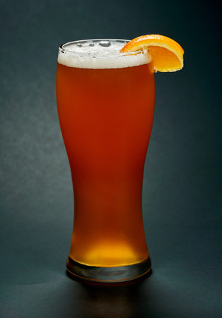 Glass of red beer with orange slice over black background. Beer is one of the oldest, most popular and widely consumed alcoholic drink in the world.の写真素材