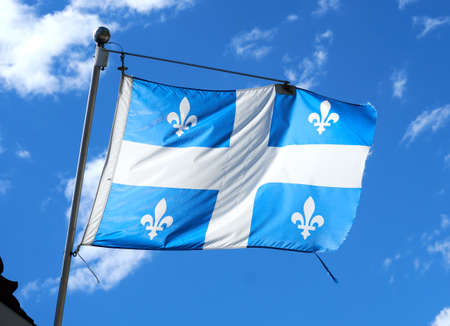 The waving flag of Quebec over a blue sky background. The flag of Quebec, called the Fleurdelise represents the Canadian province of Quebec, the flag consists of a white cross on a blue backgroundの写真素材