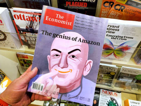 Montreal, Canada - June 30, 2020: The genius of Amazon title and a picture of Jeff Bezos as the Dr Evil on The Economist newspaper in a hand over a stack of magazines.のeditorial素材