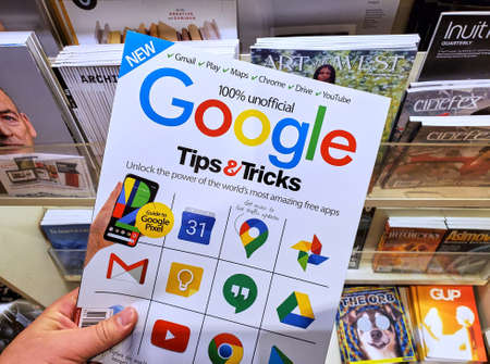 Montreal, Canada - June 30, 2020: Google Tips and Tricks unofficial magazine with Google icons on the cover in a hand over a stack of magazines.のeditorial素材
