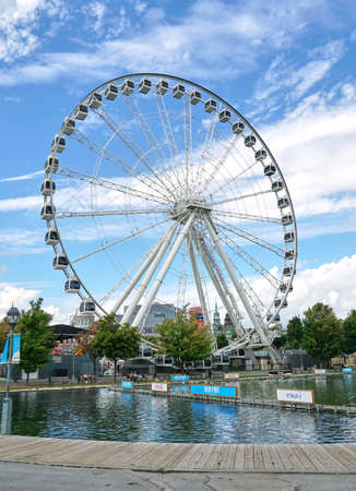 Canada, Montreal - July 11, 2021: Scenic view of ferris wheel La Grande Roue de Montreal in Old Port of Montreal over blue skies and clouds. The Old Port of Montreal is the historic port in Quebec.のeditorial素材