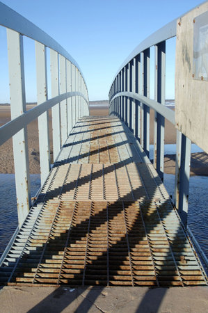 steel metal bridge on coast for pedestrians and sidelit casting shadowsの写真素材