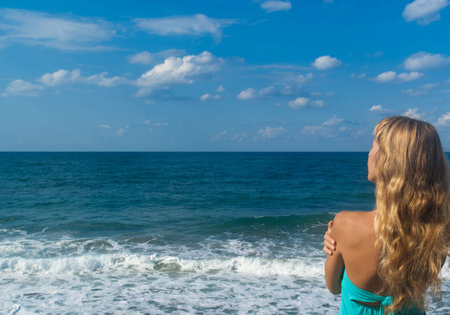 Sexy blonde woman standing on a beach and looking far on horizon