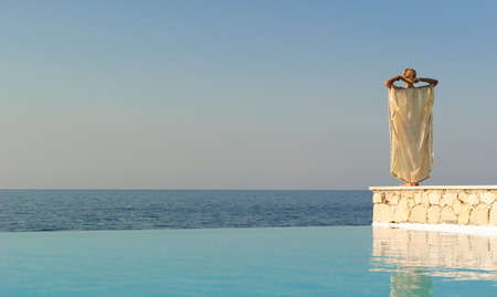 Rear view of greek style woman near infinity pool at sunsetの写真素材