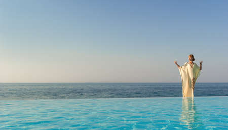 Woman in long dress like greek goddess posing near edge of infinity pool on a beachの写真素材