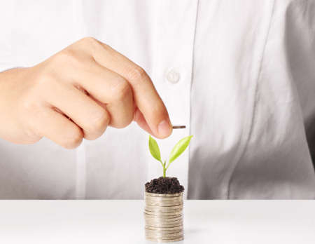 Businessman holding plant sprouting from a handful of coinsの写真素材