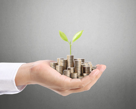 Businessman holding plant sprouting from a handful of coins 