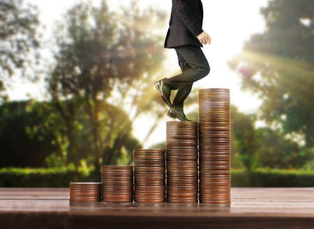 Businessman walk on stack of coins which grows success and investmentの写真素材