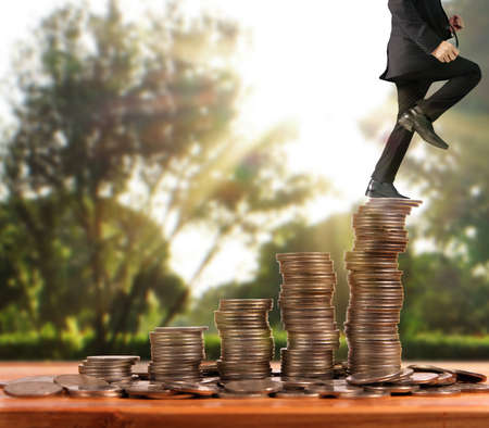 Businessman walk on stack of coins which grows success and investmentの写真素材
