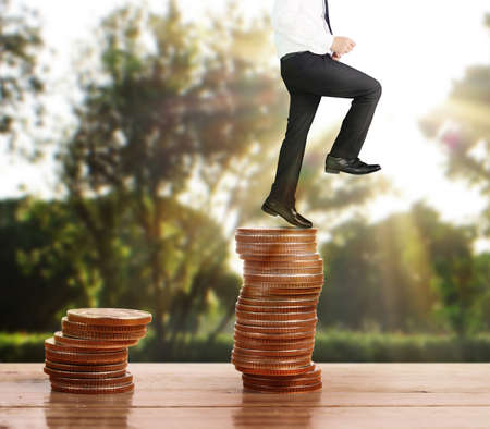 Businessman walk on stack of coins which grows success and investmentの写真素材