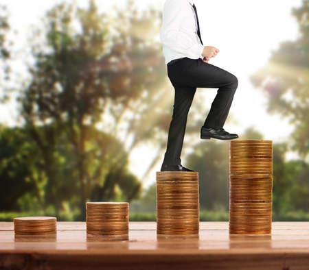 Businessman walk on stack of coins which grows success and investmentの写真素材