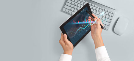 Hand holding tablet and showing holographic graphs stock market statistics gain profits. Concept of...