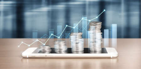 smartphone screen next to growing piles of coins and chart positive indicators in his businessの写真素材