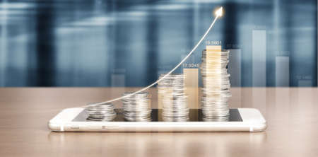 smartphone screen next to growing piles of coins and chart positive indicators in his businessの写真素材