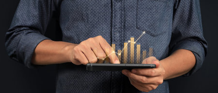 Hand holding smartphone device and touching screen. Stock exchange market concept. Trader looking on with graphs analysis candleの写真素材