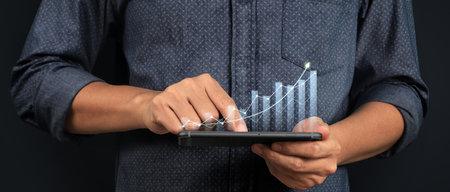 Hand holding smartphone device and touching screen. Stock exchange market concept. Trader looking on with graphs analysis candleの写真素材
