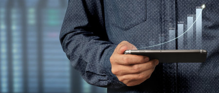 Hand holding smartphone device and touching screen. Stock exchange market concept. Trader looking on with graphs analysis candleの写真素材