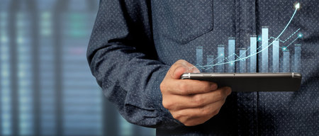 Hand holding smartphone device and touching screen. Stock exchange market concept. Trader looking on with graphs analysis candleの写真素材