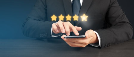 Man holding smartphone device and touching screen with five star rating feedback iconの写真素材