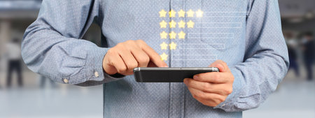 Man holding smartphone device and touching screen with five star rating feedback iconの写真素材
