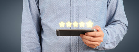 Man holding smartphone device and touching screen with five star rating feedback iconの写真素材